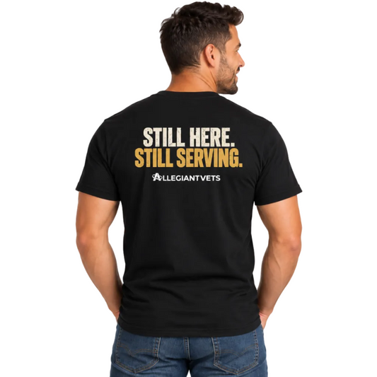 A man wearing a black t-shirt from the back, showing a graphic print that reads 'STILL HERE. STILL SERVING.