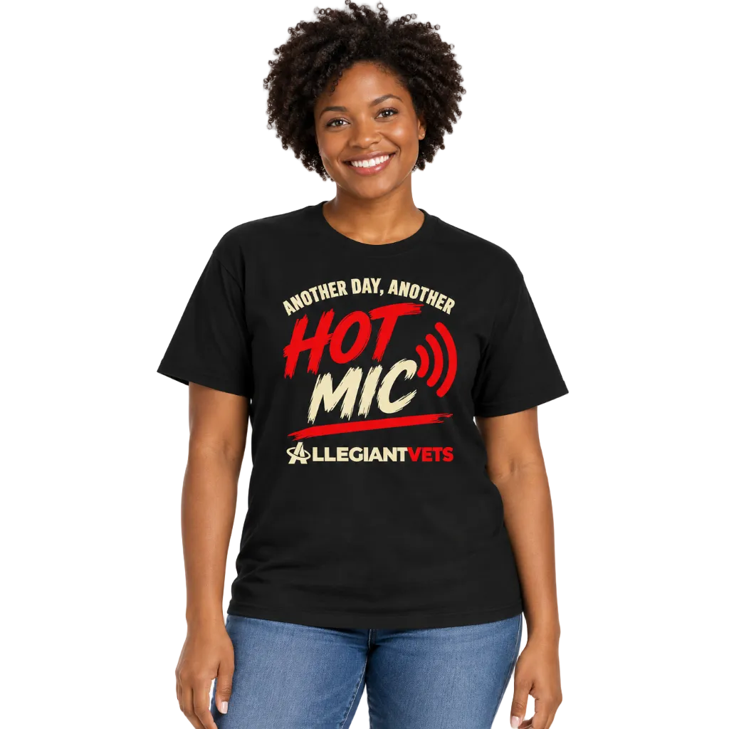 A smiling woman with short dark curly hair wearing a black graphic t-shirt and blue jeans, standing against a plain white background. The t-shirt features a red and white graphic that reads 'ANOTHER DAY, ANOTHER HOT MIC' with the 'LLEGIANT VETS' logo underneath.