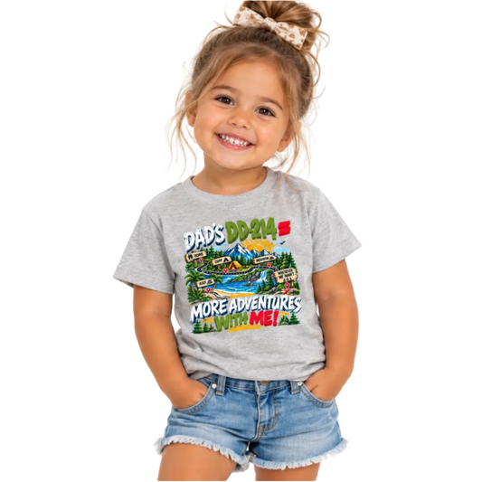 A young girl with a messy bun and bow smiling while wearing a heather gray graphic t-shirt that reads 'DAD'S DD-214 = MORE ADVENTURES WITH ME!' with a colorful cartoon landscape, paired with denim shorts, on a solid white background.