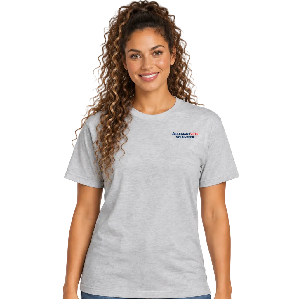A woman with long curly brown hair wearing a light heather gray short-sleeve t-shirt with a small 'AllegiantVets Volunteer' logo on the left chest, paired with blue jeans, against a plain white background.