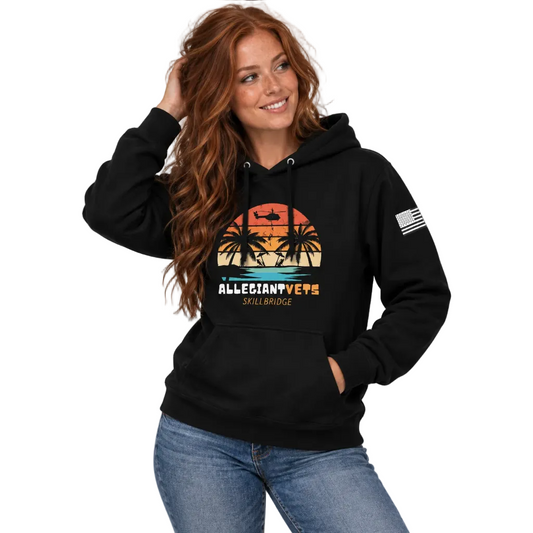 A woman wearing a black pullover hoodie with a colorful retro sunset graphic on the front that reads 'ALLEGIANTVETS SKILBRIDGE' and a small American flag print on the sleeve, paired with blue jeans.