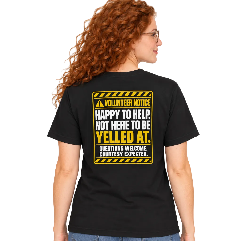 A woman with curly red hair and glasses is shown from the back wearing a black t-shirt with a yellow and white 'Volunteer Notice' graphic on the back, paired with blue jeans, against a plain white background.
